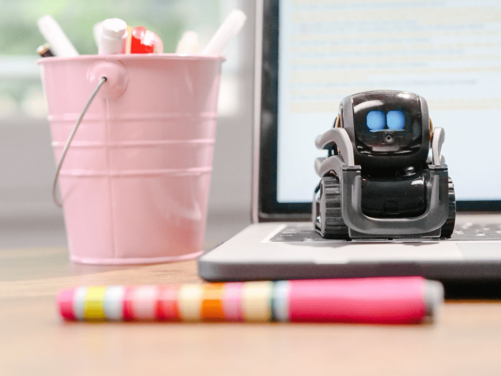 A mIniature toy robot on a laptop's keyboard and a blurred pencil in front of them